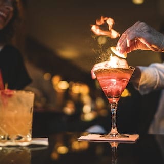 Close up of a hand adding a flourish to a flaming cocktail